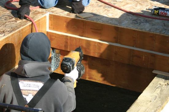 Where the plans call for a stepped-down entryway floor, a 6-inch panel is used to create the lower level. Here, the crew attaches an LVL ledger to the side of the main beam to catch the edges of the thinner panel.