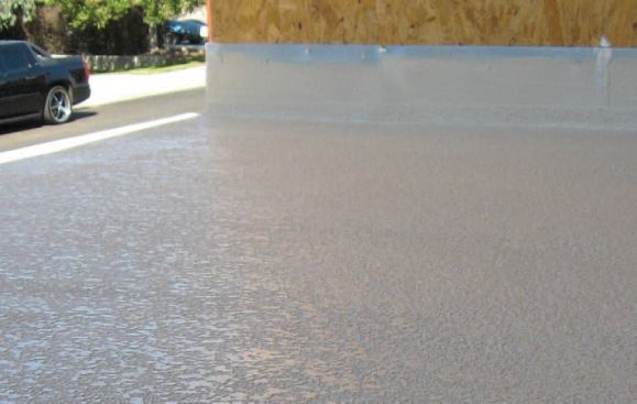 The texture is coated with pigmented concrete sealer, which dries to form a tough walkable surface. Because this deck was finished before the exterior trim was complete, it will require protection while the building paper and siding are installed.