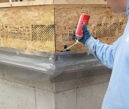 A galvanized metal flashing, air-sealed to the rim and foundation with adhesive, provides a starter strip for the foam sheathing and protects the bottom edge from burrowing bugs, rodents, and flying sparks. The attached insect screen was later folded up over the ends of the vertical vent strips behind the siding.