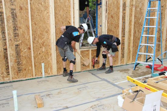 Crew member George Reefer taps a wall section into place while company owner, Chris Corson, prepares to set a powder-actuated fastener to pin the wall.
