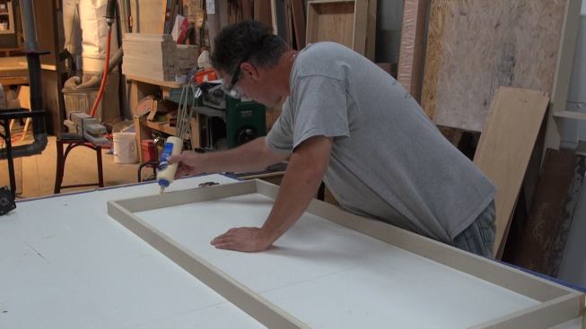 A crew member applies glue to the edge of a “REVRB” sound-absorbing panel frame in New England Soundproofing’s Waltham, Mass., cabinet shop.