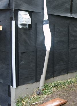 Where wider panel siding was used, a full single layer was applied, followed by 6-inch strips beneath panel joints. The vertical "streamer" is a temporary sheet-plastic downspout.