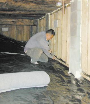 The crew applies a poly ground cover, sealed to the base of the crawlspace wall.