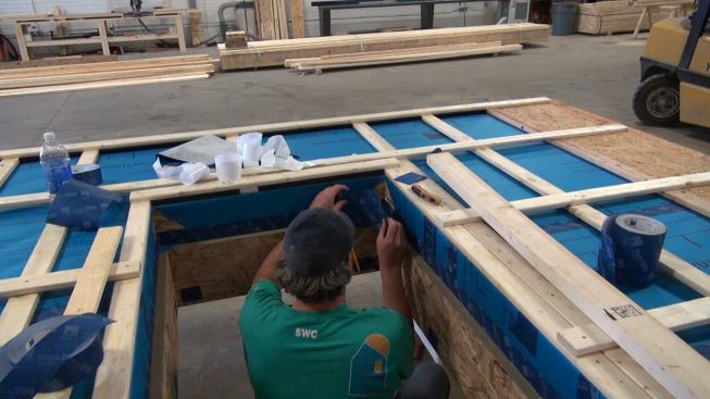 Steve Greenleaf applies ProClima Tescon Vana tape to the inside of the wall panel’s exterior window buck, integrating the weather-resistive barrier into the punched opening. The interior portion of the window buck will be detailed in the field before windows are installed. At this point, EcoCor does not build windows into wall panels before shipment because of shipping limitations.
