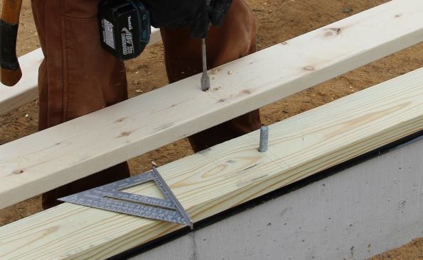 After marking the position, Hill drills bolt holes for the walk-out basement wall’s bottom plate.
