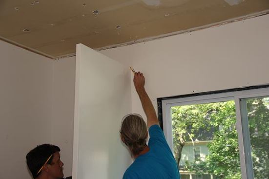With a compass and pencil, Jeff scribes the contour of the existing wall onto the end panel. He intentionally built the panel with more than an inch of extra width to allow for fine-tuning in the field.