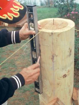 With the posts up and braced plumb, a string is used to establish the line of the beam. A carpenter uses a level to lay out the side cuts for the beam pocket.