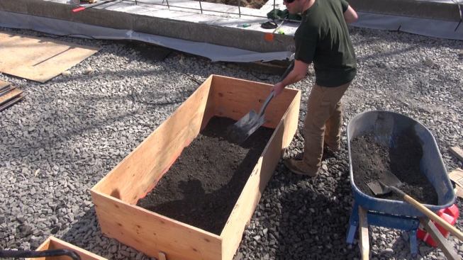 Carpenter Casey shovels “crusher run” base material into a plywood form. The crusher run contains a graded mix of fine gravel and stone dust, which compacts readily into a strong and smooth surface.