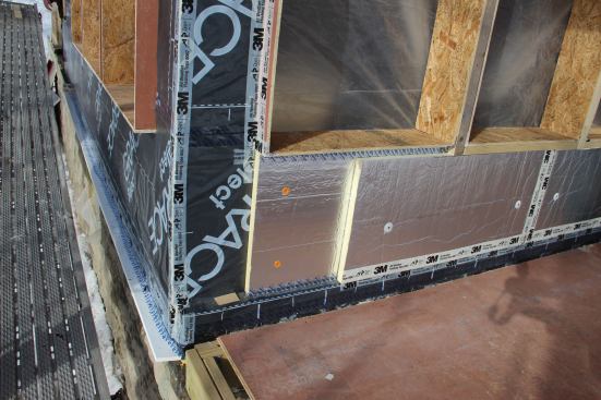 Another cutaway view of the air barrier, insulation, and window buck detail. 3M 8067 tape has been used to seal the building corner joint in the air barrier membrane, and to seal the air barrier to the window bucks. “The window bucks are part of the air barrier,” explains Pollard. Around the corner on the wall at left, window bucks have just been set and the foam installation has not yet started in this photo.