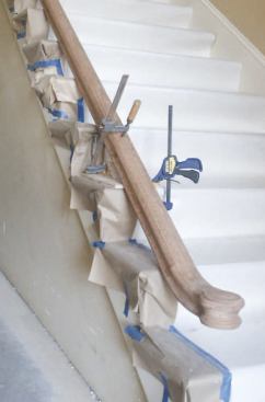 A 1 1/2-inch hole bored through the block accommodates the short bar clamp that holds the rail snug. The jig is held in place at the back with a simple expandable compression clamp made from two 5/8-inch-diameter bolts joined by a threaded rod coupler; a quick-release bar clamp holds down the front.