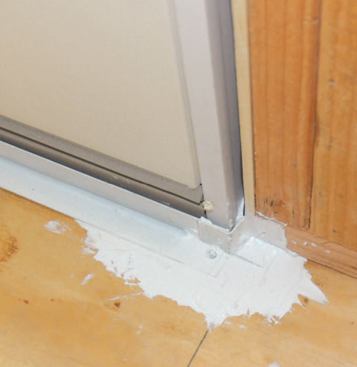 An L-shaped metal dam embedded in sealant and fastened to the floor after the door is installed directs water toward the drainage gap.