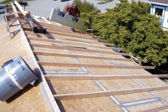 To provide added insulation with minimal thermal bridging, 2x4 sleepers were laid edgewise on the roof sheathing, staggered between rafters, and allowed to extend past the plane of the walls to form wide overhangs.