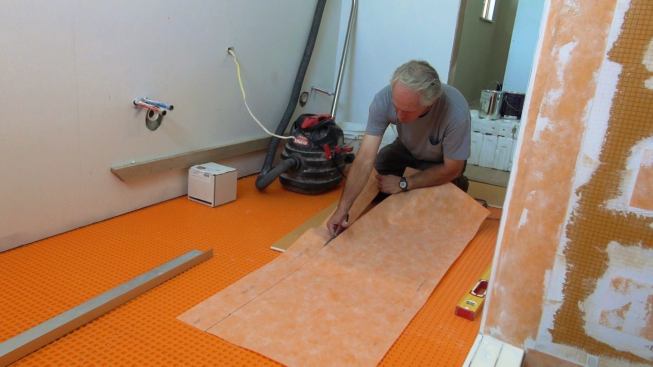 Boucher cuts Kerdi membrane to width before adhering it to the built-up curb. The membrane will be layered onto a mortar bed over the curb to create a waterproof substrate for tile.