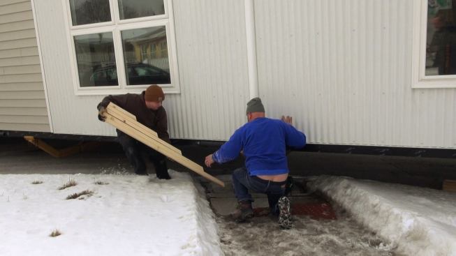 Steve Davis and Tyler Boice place a lumber ramp in front of the trailer wheels in order to help the modular unit get past a curb as the rig exits the roadway and enters a driveway.