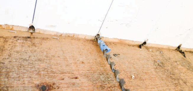 To stop air penetration at the gable overhang of a T&G cathedral ceiling, a 3/4-inch bit is used to bore holes where the boards cross the outermost pair of rafters.
