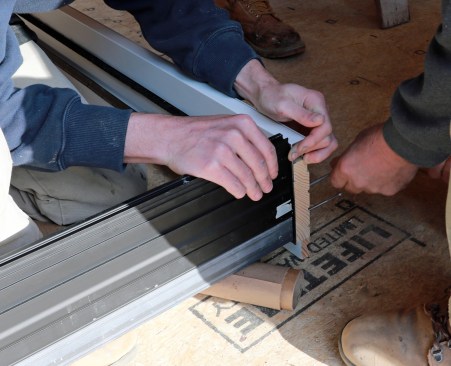 The threshold must be secured to the side jambs. Note the exposed end grain of the side jamb. This must be sealed. The crew seals it with flashing to stave off any potential rot.