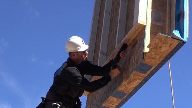 Adhesive sealant is applied to panels at the last moment, just before the panels are placed. Here, company owner, Chris Corson, applies a bead to the underside of the wall plate of a second-story gable end wall section as the wall panel hangs suspended from the crane.
