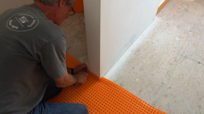 Boucher trims a piece of Ditra to fit around the base of a half-wall partition between the toilet and the main bathroom.