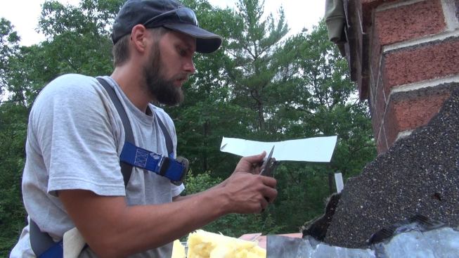 After noting the location of some data cable by feel, Phillips bends a piece of metal around the sharp edge of the flashing in order to protect the wire insulation from damage.