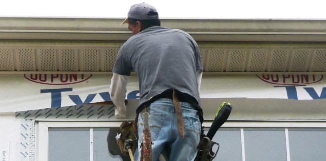 A worker lifts the StuccoWrap along the top of the wall to tape the top fin of the window to the sheathing.