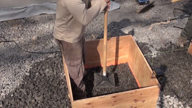 Carpenter Tim compacts the trap rock sub-base inside the plywood pad footing form.