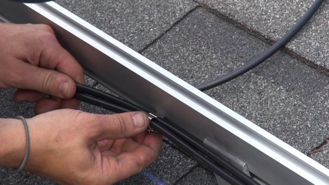 Before the crew begins to mount panels, Janarelli clips the “home run” conductors for the panel arrays into a groove on the aluminum mounting bracket. Each panel comes pre-wired with plug-in connectors so that the panels can be connected in series to create a “string.” When the strings are assembled, the home-run conductors will be connected at the beginning and end of each string, and DC power will begin flowing to the inverter in the garage.