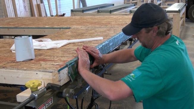 Steve Greenleaf applies ProClima Extoseal membrane tape to the underside of the 2x4 inner wall plate for the panel. Extoseal is designed as a moisture-barrier tape for junctures between wood members and concrete foundation elements or other moisture sources. This plate will contact the slab foundation when the wall is set. However, the slab itself will also be isolated from ground moisture by an EPS insulating form system and a sheet of heavy-duty polyethylene.
