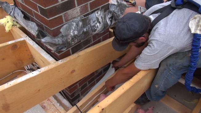 Working at close quaters, Phillips wiggles a piece of metal flashing into place at the opening where the brick chimney penetrates the ceiling framing. With the roof sheathing removed and the ceiling exposed from above, according to Phillips, this is a relatively easy situation: often, the chimney-to-framing gap is less accessible.