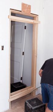 The jamb assembly is held in the opening between scraps of strapping. A temporary spreader near the bottom maintains a uniform finish opening. The author first cuts the side jambs to compensate for an out-of-level floor.