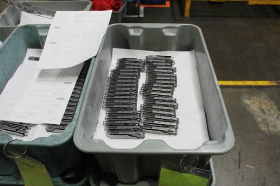 These side handles for the Wave 2 were punched, folded, and formed by the progressive press in the previous photo. Note the paperwork that goes with the parts; it contains a description as well as a bar code that allows the company to track the progress of components as they go through the factory.