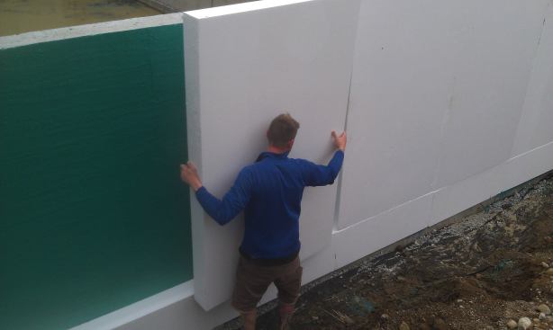 Chris Corson applies 6-inch polystyrene foam insulation to the basement wall after forming, pouring, and waterproofing the basement walls.