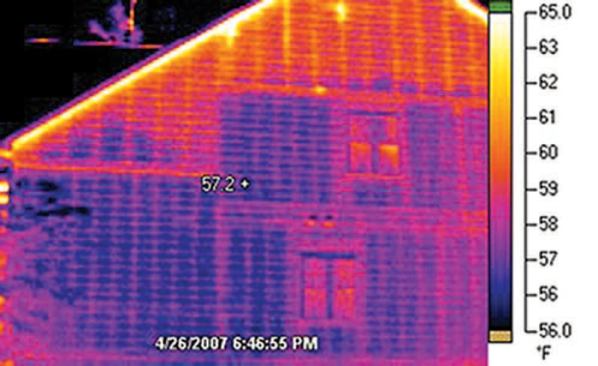 The air-conditioned living space in the structure can clearly be distinguished from the uninsulated attic; although the image was taken after dark, the framing in both areas is visibly warmer than the fiber-cement siding, because it retains heat from the warm day.
