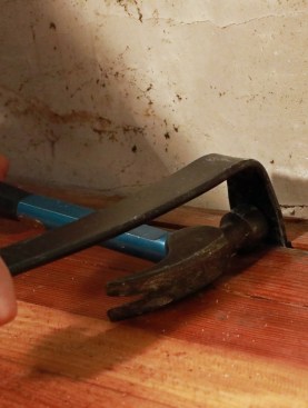 To loosen up a floor board, the author drives a flat bar into the gap and pushes it away from the tongue on the next board. Note that you can strike the bar in the "opposite" direction to push the boards apart.