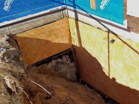 We sealed the connection to the sill plate with a site-bent flashing. We added a generous bead of Henry Moistop Sealant to the bottom edge of the sheathing, then set the flashing into that. We topped it all with tape and then Henry Blueskin peel-and-stick WRB.