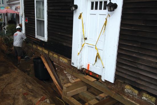 To create room to stack cribbing, we hand-dug pocket holes about 4 feet deep, undercutting the foundation near the corners and at the center. After stacking the cribbing, we used bottle jacks to raise the building just enough to slide in short lengths of 6x6s directly under the existing sill.