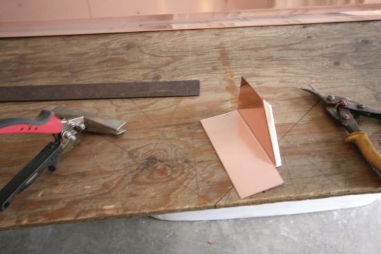 Tin snips and hand brakes are used to fabricate the corner pieces from copper step-flashing.