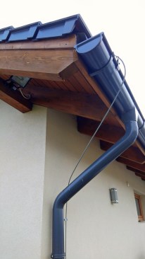 Downspouts are typically formed from a much sturdier 1.6-mm (16-gauge) metal. Note the steel flashing visible near the end of the gutter that directs water away from the fascia from blowing rain. The cable is a ground wire from lightning rods. The roofing here is flat, glazed concrete tiles. We are seeing the profile specific to rake edges.