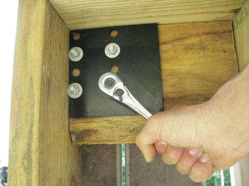 TimberTech/Azek’s reinforcing plate is predrilled with eight holes (two pairs of four holes) positioned near one corner of the plate, to match the pattern in the base plate. This arrangement enables the plate—and the post above—to be located close to the rim joist and a deck joist. The same plate design is used to reinforce the blocking on the Vinylast and UltiMount posts. The post must be oriented such that the bolt holes clear the rim joist and deck joist by at least 1/4 inch so the base plate will fit.