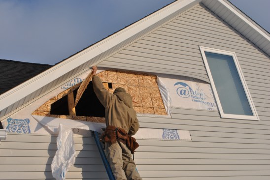 Working from outside, a carpenter cuts into unheated space above the garage next to the bonus room