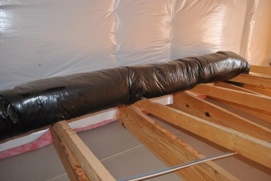 Under the low roof, he finds the back of the bonus-room wall, with a plastic air barrier stapled to the wall over the fiberglass insulation (but not sealed at the top or the bottom).
