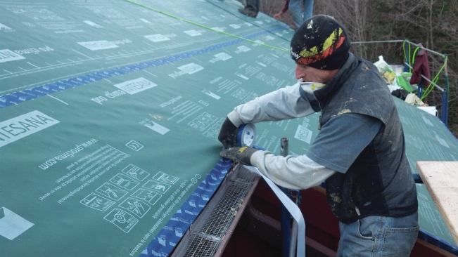 A worker seals a vapor-permeable weather barrier membrane with tape as part of an extensive roof retrofit.