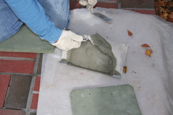 Grout mortar is mixed to the same proportions as setting bed mortar, but in a slightly drier mix. The author uses a margin trowel to spread it in a patty about ½-in. thick on his hawk. Tapping the handle of the hawk on a hard surface drives the  mud onto the surface of the hawk and helps hold it in place. 