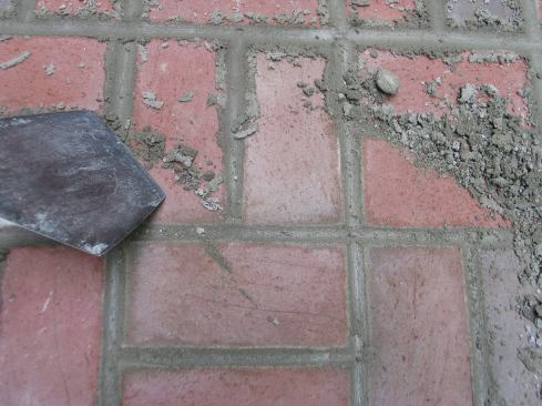 After allowing the grout to harden for about a day, the author used a bucket trowel, which has the front half cut off square, to break off the fins on the joints, then swept up the crumbs of mortar.