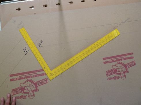 For laying out the angled joists and the hips, a framing square is placed at a 5-in-12 pitch on the line representing the outside edge of the wall. The lines are extended to the back of the bay using a long straightedge held against the square's blade.