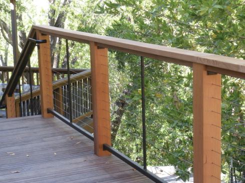 When wood posts and rails are used, a structural subrail is needed to resist the compressive force of the tensioned cables.