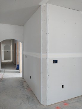 After hanging the drywall, workers trim the corner with a pair of splayed adjustable plastic corner beads and then mud the joints.