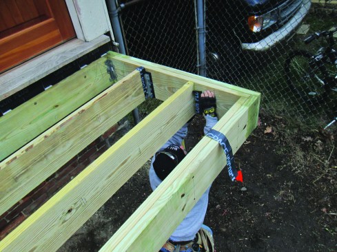 The author applies strips of flashing membrane to PT framing before installing joist hangers and other hardware.