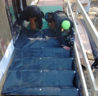 Working from the center, workers use cap fasteners to attach the membrane to the joists.