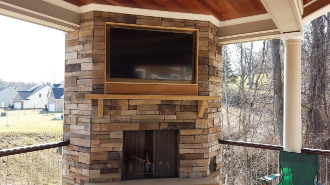 When you’re installing an outdoor TV above a fireplace, the author recommends locating it close to a mantel that projects at least 10 inches to help divert heat away from the TV, with the mantel no higher than 5 feet above the floor to preserve viewing angles.