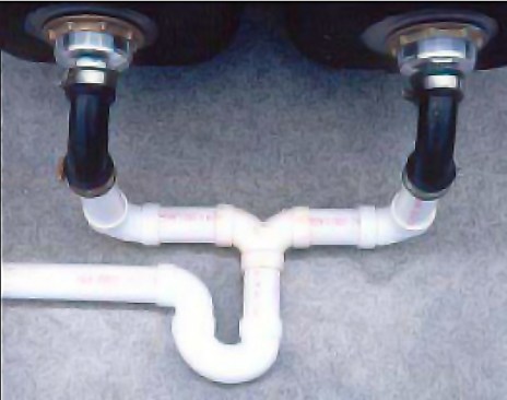 For a leakproof drain and trap assembly, the author uses glued plastic fittings and places the pipes at the back of the sink cabinet. The rubber 90-degree elbows, attached with hose clamps, allow for quick disassembly.